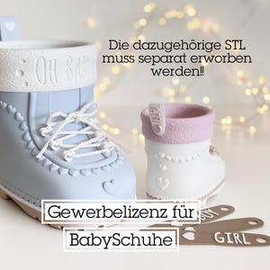 May include: Two decorative baby bootie-shaped containers, one light blue and one white, with pink trim. The blue bootie has the text "OH BABY" and white laces. The image also includes metal tags that say "BOY" and "GIRL".