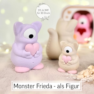 Può includere: Una statuina di mostro viola chiaro con un solo occhio e un cuore rosa. Una statuina di mostro beige più piccola con un cuore rosa è di fronte a una scultura beige. Il testo "Monster Frieda - als Figur" è in basso.