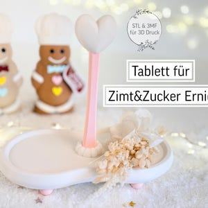 May include: A white and pink serving tray with a heart-shaped top and a decorative floral arrangement. Two gingerbread men in chef hats stand in the background. The text on the image reads "Tablett für Zimt&Zucker Ernie."