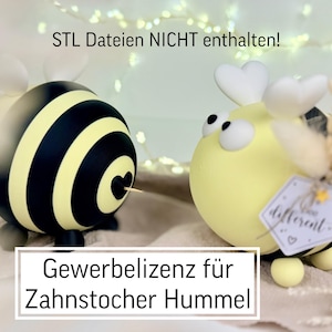 Può includere: Due portastuzzicadenti decorativi a forma di ape. Un'ape è gialla e a strisce nere, l'altra è gialla con dettagli neri. Il testo "Gewerbelizenz für Zahnstocher Hummel" è in un rettangolo bianco.