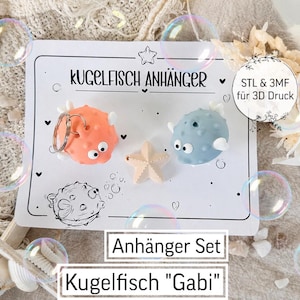 Könnte beinhalten: Ein Set aus orangefarbenen und blauen Kugelfisch-Schlüsselanhängern mit einem Seestern, präsentiert auf einer weißen Karte mit deutschem Text. Die Karte lautet "Kugelfisch Anhänger" und "Anhänger Set Kugelfisch 'Gabi'". Blasen und dekorative Elemente umgeben das Set.