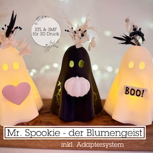 May include: Three illuminated ghost-shaped decorations. One has a pink heart, another a white pumpkin, and the third has a "BOO!" sign. Each ghost is topped with floral accents. The text "Mr. Spookie - der Blumengeist" is at the bottom.