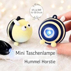 May include: Two bee-shaped mini flashlights, one yellow and black, the other navy blue and yellow, with a small black remote. The text "Mini Taschenlampe Hummel Horstie" is displayed below the flashlights. The flashlights have a light-up feature.