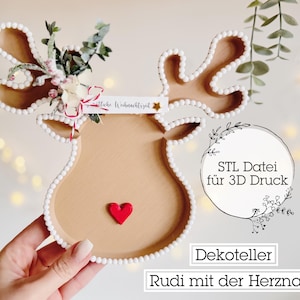 May include: A reindeer-shaped decorative tray with a red heart nose and white beaded trim. The antlers are decorated with greenery and flowers. Text on the tray reads "Frohe Weihnachtszeit" and "Rudi mit der Herznase".