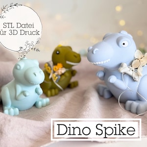 Peut inclure: Trois figurines de dinosaures bleus et verts sont présentées sur une surface rose-beige. Le texte "Dino Spike" est dans un cadre blanc. Une figurine a un accessoire en forme d'os. L'image comprend également le texte "STL Datei für 3D Druck".