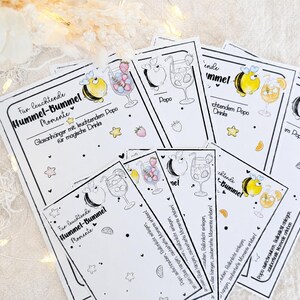 May include: A collection of rectangular white paper cards featuring black line art illustrations of bumblebees and cocktail glasses. The text reads "F&uuml;r leuchtende Hummel-Bummel Momente" and "Glasanh&auml;nger mit leuchtendem Popo f&uuml;r magische Drinks" with small yellow star and fruit accents.