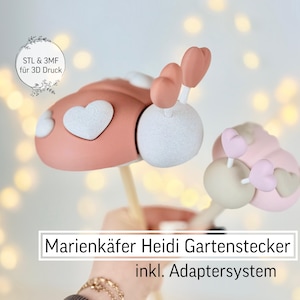 May include: Two decorative ladybug garden stakes. The larger ladybug is pink with white heart accents and a white head. The smaller ladybug is light pink with a beige head and heart accents. The text "Marienkäfer Heidi Gartenstecker inkl. Adaptersystem" is visible.