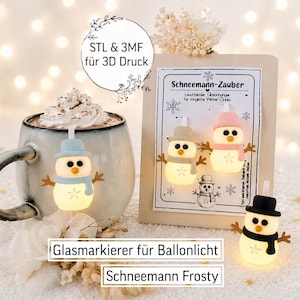 Könnte beinhalten: Drei kleine, leuchtende Schneemann-Anhänger mit Hüten und Schals in Blau, Rosa und Schwarz. Ein Anhänger hängt an einer Tasse mit Getränk, zwei weitere sind auf einer Karte mit der Aufschrift Schneemann-Zauber befestigt.