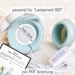 May include: A light blue and white lamp component with a textured edge and a circular light insert measuring max. 6cm. The set includes a white power cord with a four-button controller and a printed instruction sheet labelled passend f&uuml;r Lampenset 001.