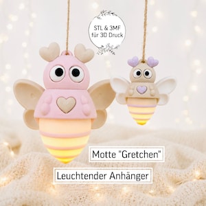 May include: Two hanging insect-shaped ornaments with large eyes, heart-shaped antennae, and glowing striped abdomens. The larger ornament is pink, and the smaller one is beige. Text reads: STL & 3MF für 3D Druck, Motte Gretchen, Leuchtender Anhänger.