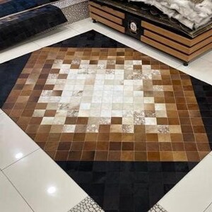 May include: A brown and black patchwork rug made of cowhide. The rug has a diamond shape with a black border and a white and brown center.