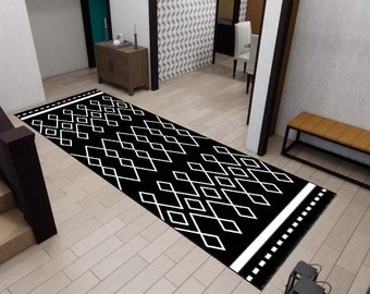 May include: Black and white geometric patterned rug with fringe on the ends. The rug is laid out on a black and white tiled floor in a hallway.