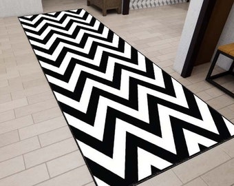 May include: Black and white chevron patterned rug with a geometric design. The rug is placed on a tiled floor in a hallway.