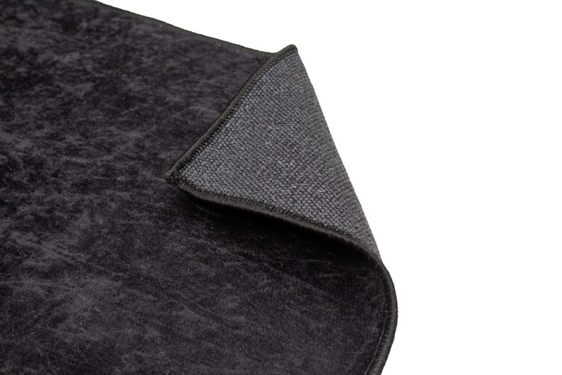 May include: Close-up of a black rug with a textured surface. The rug has a black border and a grey backing.