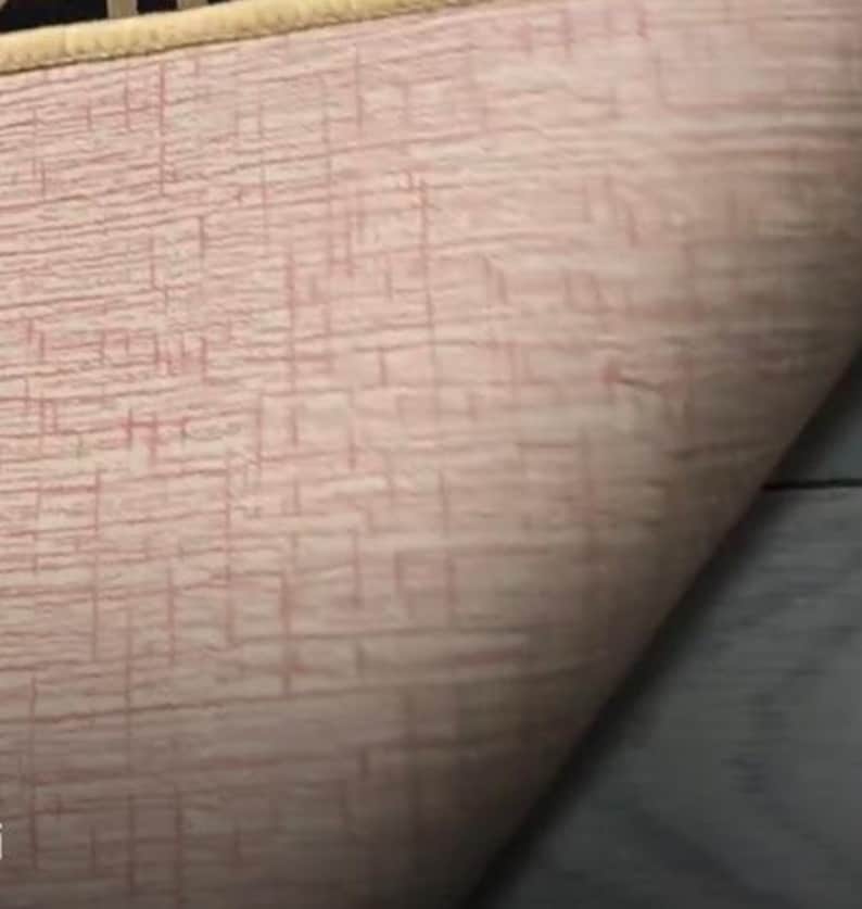 Puede incluir: Primer plano de la parte posterior de una alfombra rosa y blanca con un patr&oacute;n tejido. La alfombra tiene un borde de color crema.