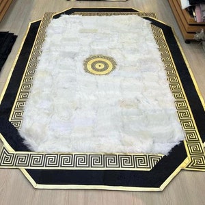 May include: A white fluffy rug with a black and gold border. The border features a repeating Greek key pattern.