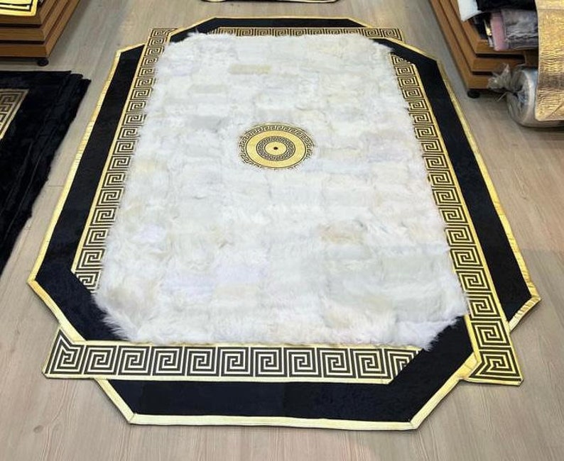 May include: A white fluffy rug with a black and gold border. The border features a repeating Greek key pattern.