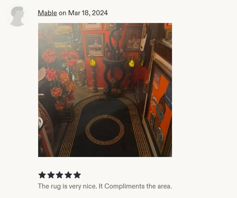 Puede incluir: Una alfombra negra con un borde dorado de patr&oacute;n de greca y un motivo circular central. La alfombra es rectangular con extremos redondeados y est&aacute; colocada en el suelo de una habitaci&oacute;n con paredes naranjas, muebles y decoraci&oacute;n floral.
