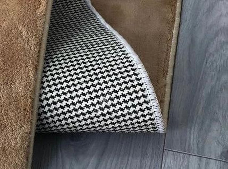 May include: A brown rug with a black and white patterned backing. The rug has a fringed border.