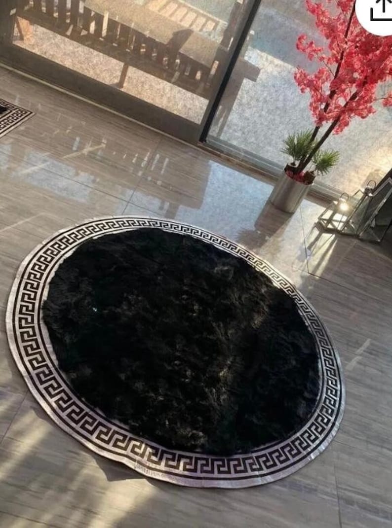 May include: A black and silver round rug with a Greek key border. The rug is made of a soft, fluffy material.