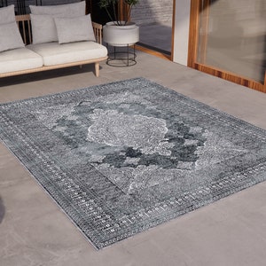 May include: A grey and white patterned rug with a vintage design. The rug is laid out on a concrete floor in a modern living space.