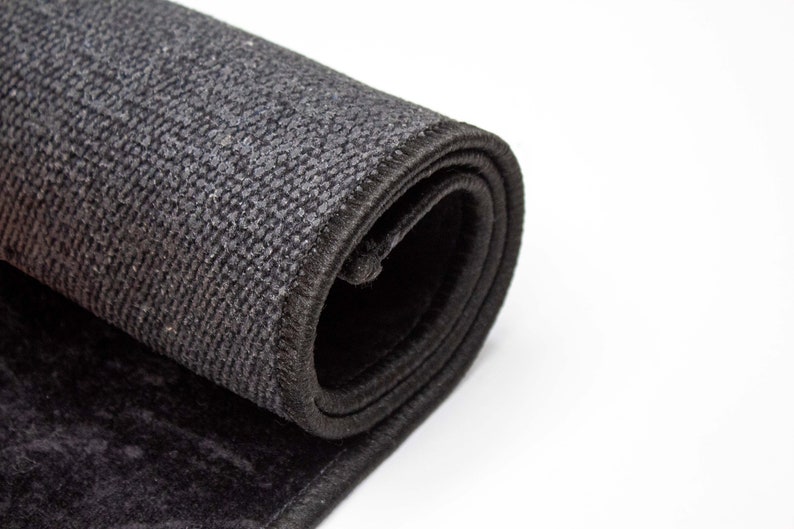 May include: Close-up of a rolled-up black rug with a textured surface. The rug is rolled up tightly and the edges are visible.