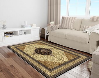 May include: Rectangular area rug with an ornate floral design. The rug features a central medallion in black and brown, surrounded by beige and gold patterns. A black border frames the rug, which is placed on a hardwood floor.