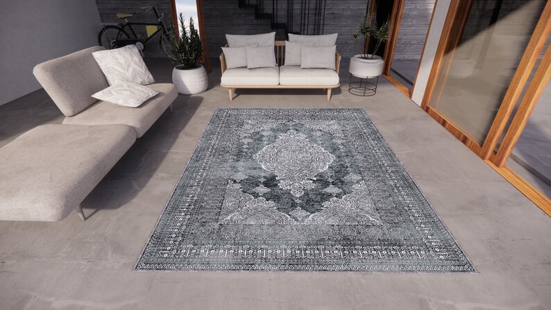 May include: A grey and white patterned rug with a vintage design. The rug is laid out on a concrete floor in a modern living room setting.