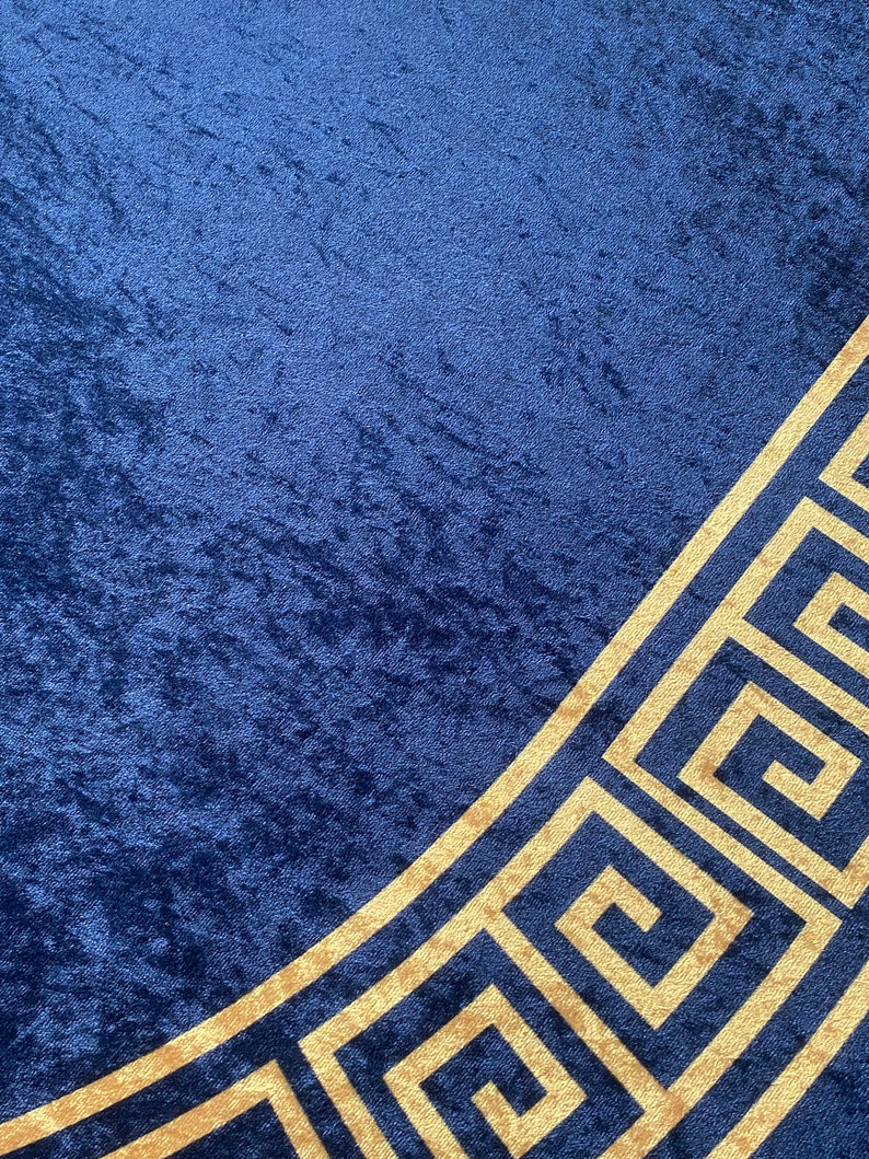 Puede incluir: Una tela azul profundo con textura de terciopelo arrugado que presenta un prominente patr&oacute;n de llave griega de color dorado que corre diagonalmente por la esquina inferior derecha. El material muestra un brillo rico con tonos variados.