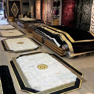 May include: A shop display featuring a variety of rugs with black and gold geometric patterns. The rugs are arranged on a wooden floor and some are stacked on top of each other.