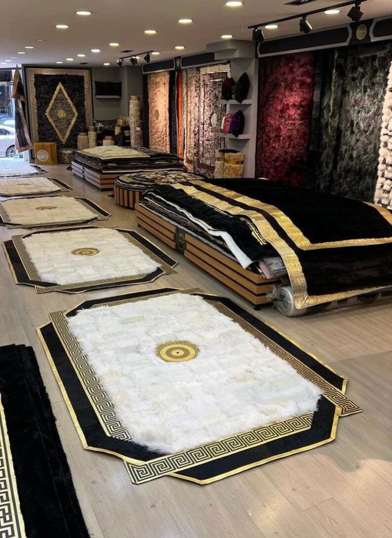 May include: A shop display featuring a variety of rugs with black and gold geometric patterns. The rugs are arranged on a wooden floor and some are stacked on top of each other.