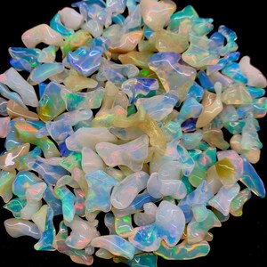 以下が含まれることがあります： 様々な形と大きさの虹色のオパールチップのコレクション。チップは白、青、黄色のミックスです。