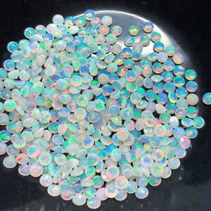 May include: A large pile of white opal gemstones with iridescent rainbow colors. The opals are round and have a smooth, polished finish.