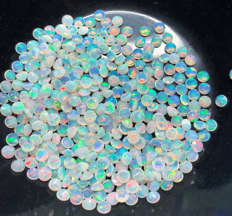 May include: A large pile of white opal gemstones with iridescent rainbow colors. The opals are round and have a smooth, polished finish.