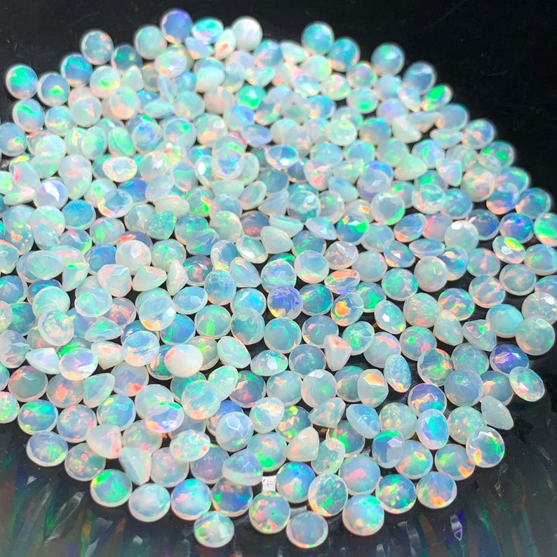 May include: A large group of white opal gemstone cabochons with iridescent rainbow flashes. The stones are round and have a smooth, polished finish.