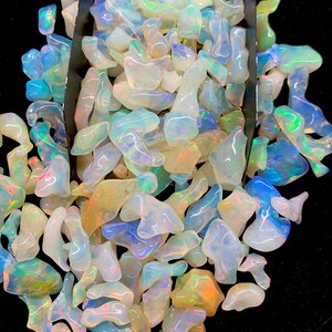 以下が含まれることがあります： 様々な形と大きさの虹色のオパールチップが大量に積み重ねられています。チップは白、青、緑、黄色の混合です。