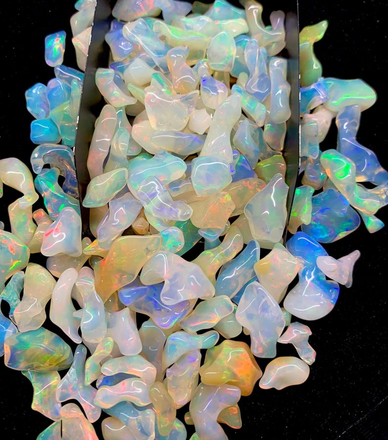 以下が含まれることがあります： 様々な形と大きさの虹色のオパールチップが大量に積み重ねられています。チップは白、青、緑、黄色の混合です。