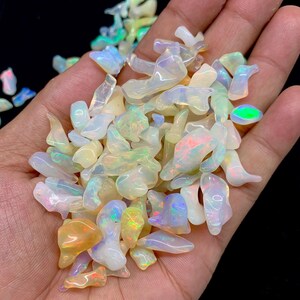 以下が含まれることがあります： 様々な形と大きさの虹色のオパールチップのコレクション。チップは白、黄、オレンジのミックスで、虹色の光沢があります。