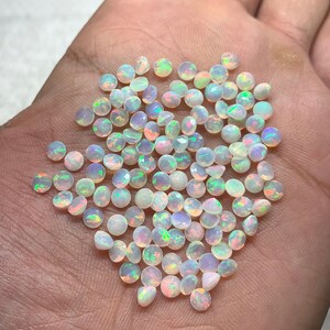 May include: A pile of small, round, white opal gemstones with iridescent rainbow colors.