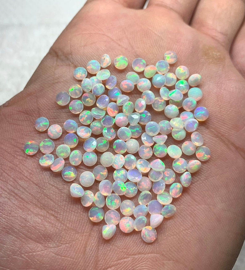 May include: A pile of small, round, white opal gemstones with iridescent rainbow colors.