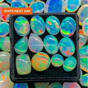 Può includere: Una collezione di 12 pietre preziose di opale di forma ovale e a goccia in una scatola di velluto nero. Gli opali sono iridescenti con bagliori di verde, blu, arancione e rosso.