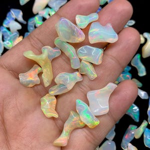 以下が含まれることがあります： 様々な形と大きさの虹色のオパールチップのコレクション。チップは白、黄、オレンジの色合いで、虹色の輝きを放っています。