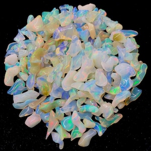 以下が含まれることがあります： 白、青、緑の様々な色合いの虹色のオパールチップが大量に積み重ねられています。チップは不規則な形をしていて、半透明な外観をしています。