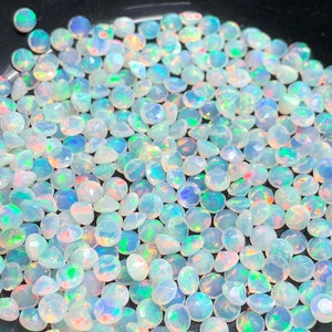 May include: A large pile of iridescent white opal gemstones. The opals are round and have a faceted cut.