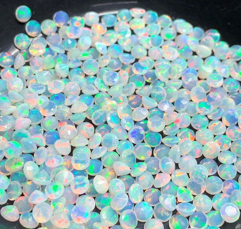 May include: A large pile of iridescent white opal gemstones. The opals are round and have a faceted cut.