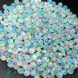May include: A large group of iridescent white opal gemstones, each with a round, faceted shape. The opals are scattered on a black surface.