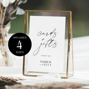 May include: A white sign with black calligraphy that reads "cards + gifts" in a gold frame. The sign also includes the text "Thank You Andrew and Lucy".
