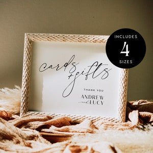 May include: White sign with a wood-like frame, with the text "cards + gifts" in black cursive script. Below the text is "Thank you Andrew and Lucy". The sign is on a tan fabric surface. A black circle with white text says "Includes 4 Sizes".