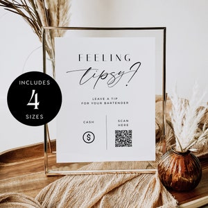 Può includere: Un cartello bianco con testo nero che dice "Feeling Tipsy? Leave a tip for your bartender. Cash or Scan Here." Il cartello è in una cornice dorata e si trova su un tavolo di legno con un vaso marrone e erba di pampa secca.