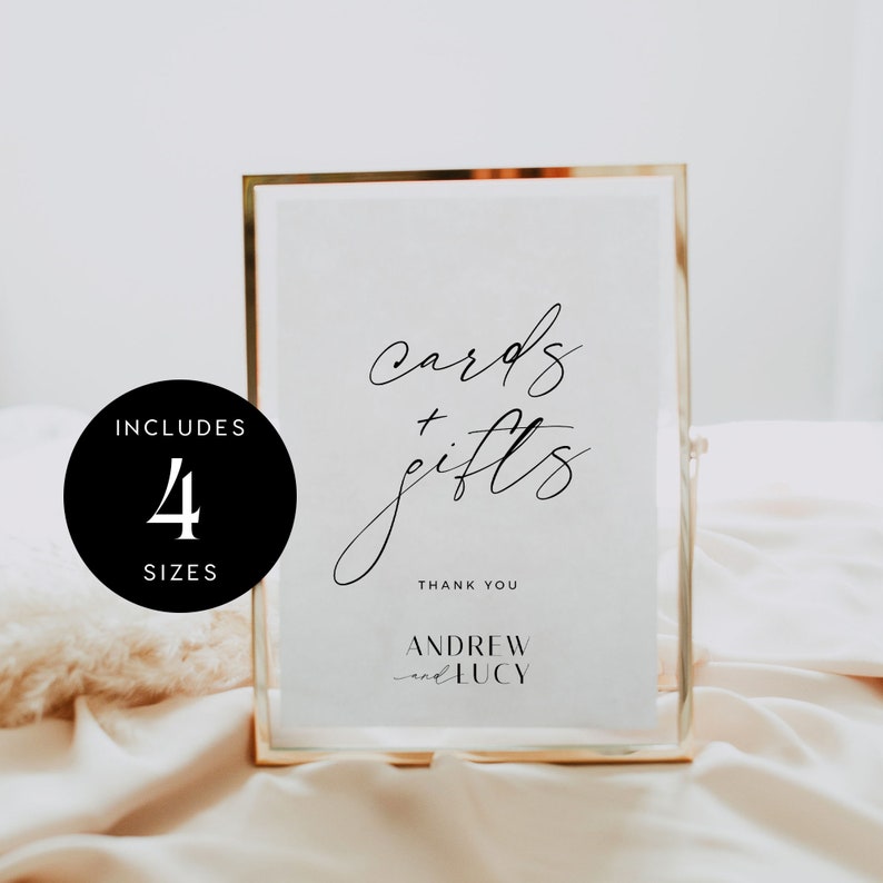 May include: A gold-framed sign with white background and black text that reads "cards + gifts" with the names "Andrew and Lucy" below. The sign is on a white and gold surface. The sign includes four sizes.